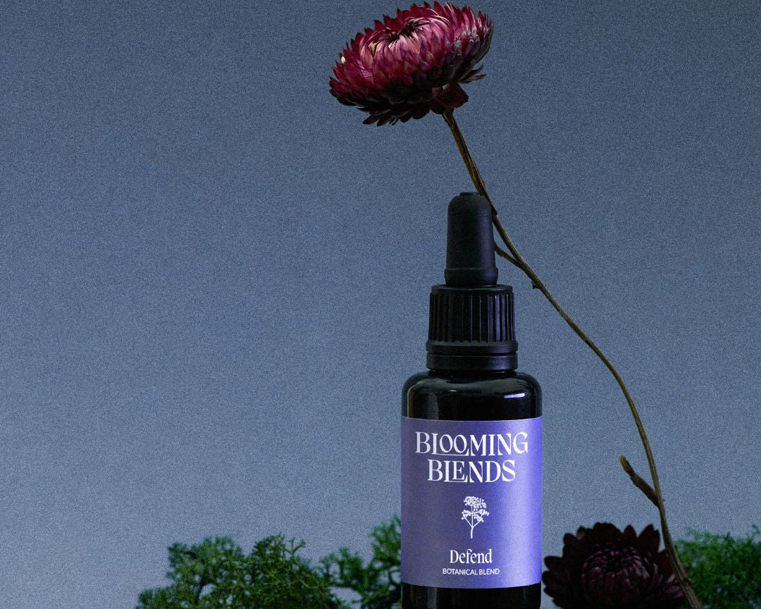 Blooming Blends Defend tincture bottle with a dark red flower on a blue background